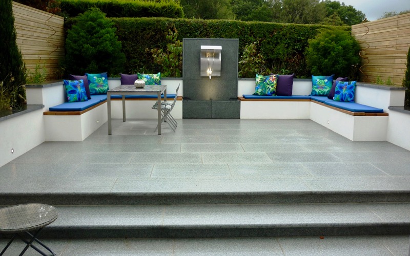 Sunken garden with full width granite steps leading up to a paved terrace with a bespoke water feature with benches containing storage 